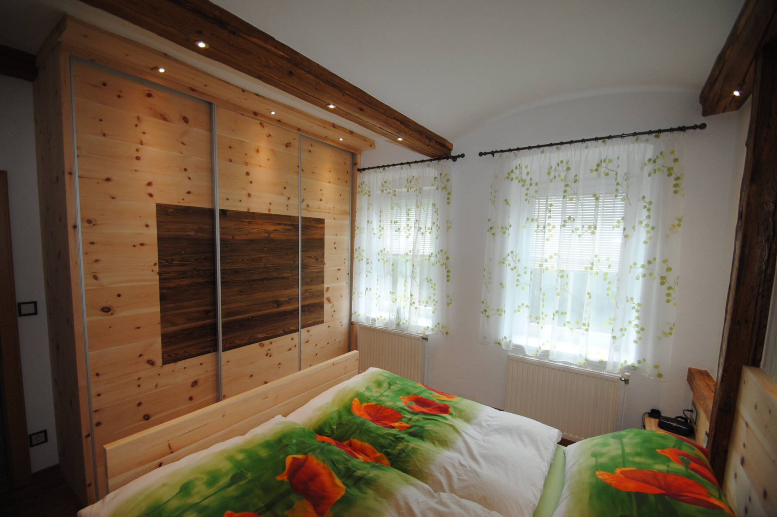 Schlafzimmer mit Bettrückwand aus Altholz und sichtbaren Holzbalken an der Decke